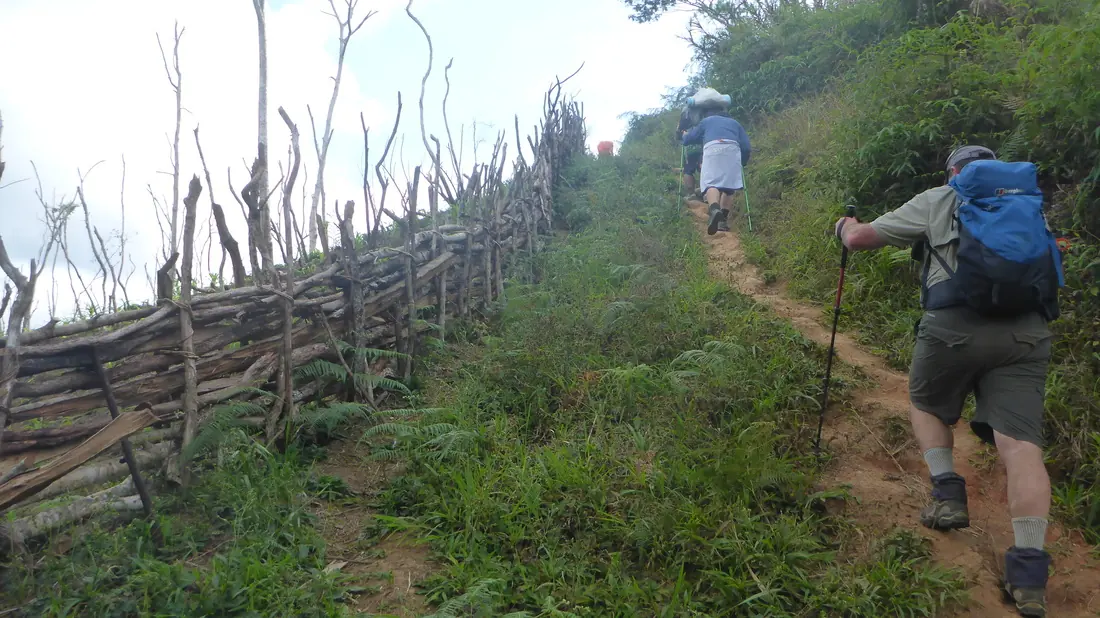 A trekker climbing past a village fence